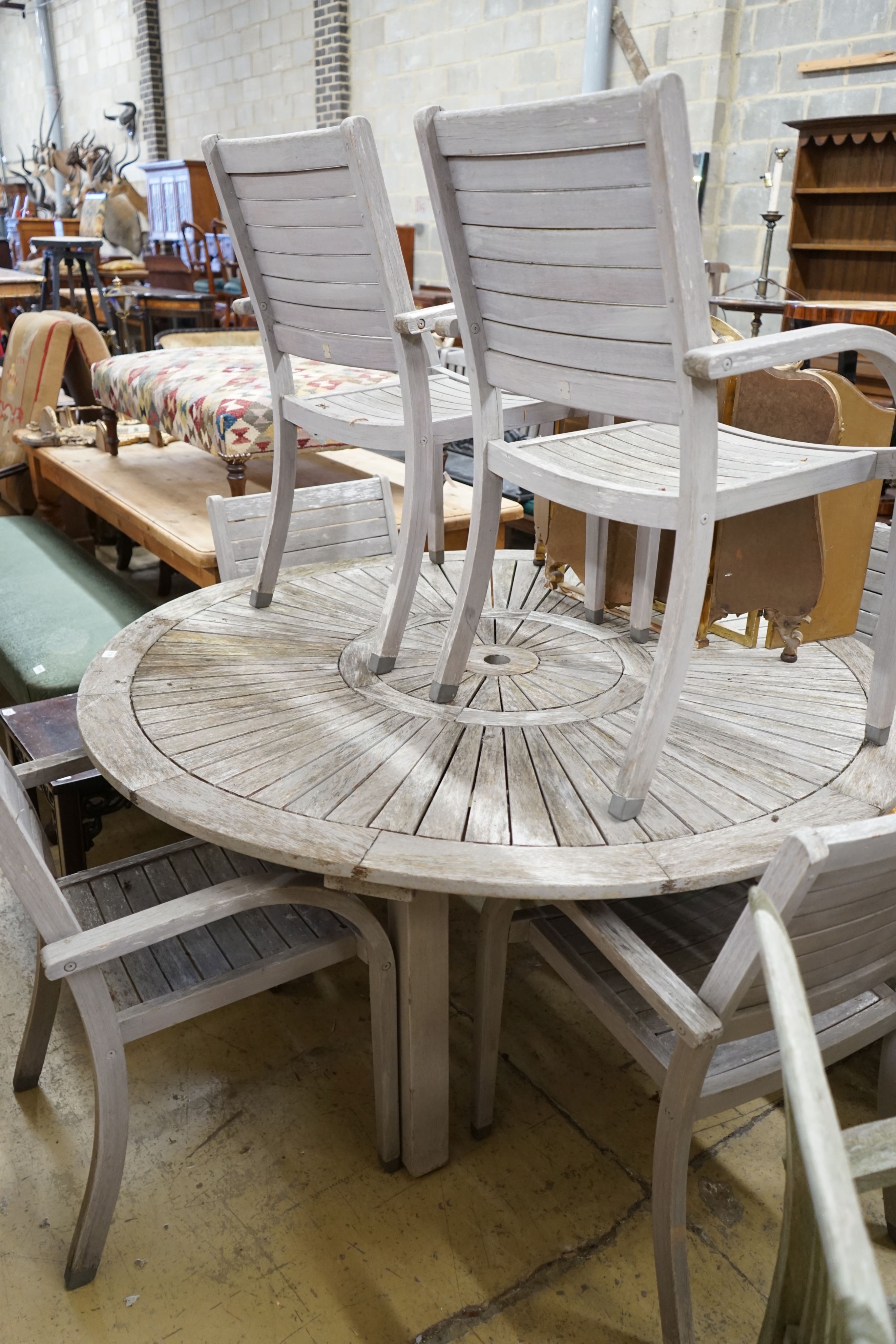 A circular weathered teak garden table, diameter 153cm, height 75cm together with six weathered teak stacking garden elbow chairs